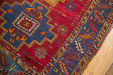 Corner of vintage Turkish rug with cherry red field, royal blue stepped medallion, colorful serrated border.