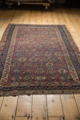 Lower corner of antique Malayer rug, showing plum field, dark navy borders, and repeating floral blossoms.