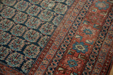 Close-up of antique Heriz rug's navy boteh field and complex terracotta border patterns.