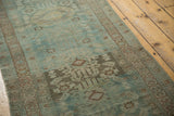 Distressed Hamadan runner with faded teal field, worn texture, and intricate bronze border.