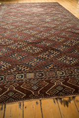 Antique Turkmen carpet's geometric hook gul motif, detailed border, and worn aubergine, navy, ivory pile.