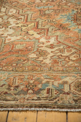 Distressed Heriz carpet's low pile, geometric pattern, dusty bronze, faded teal, and fringe.