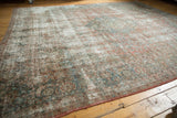 Distressed vintage Kashan carpet, worn pile and visible foundation with muted floral colors.