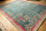 Distressed corner of Art Deco rug, faded sky blue field, pink-red border, and worn floral motifs.