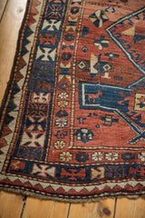 Antique Caucasian rug's corner with geometric borders, brick red pile, and worn fringe.