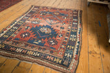 Antique Caucasian rug's lower corner, geometric brick red, navy, ivory patterns, and secured fringe.
