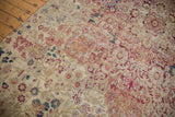 Close-up of antique Kermanshah carpet's mil fleur field, showing muted red, blue, and ivory motifs.
