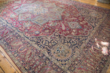 Antique Kerman rug corner detail: navy cartouche border, plum field with scrolling florals.