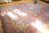 Antique Kerman carpet's intricate scrolling vinery, floral bouquets, and layered borders in deep red, navy, ivory.