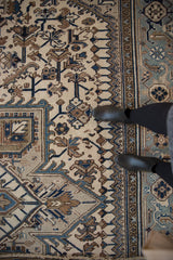 Distressed vintage Heriz carpet showing geometric patterns and border in ivory, blue, and brown.