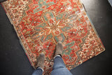 Distressed vintage Heriz rug showing geometric motifs and worn texture in brick red, teal, ivory.