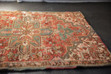 Distressed Heriz rug showing worn geometric floral pattern in brick red, teal, and visible polychrome selvage.