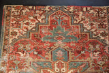 Distressed vintage Heriz rug detail showing geometric palmette, red, teal, ivory colors, and visible wear.