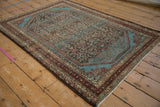 Angled view of a distressed Malayer rug's worn Herati pattern and brilliant blue spandrels.