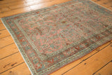 Distressed Sarouk rug showcasing intricate floral motifs in dusty raspberry and ocean blue-green hues.