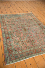 Distressed Sarouk rug corner shows intricate floral patterns and worn pile in dusty red, ocean blue-green.