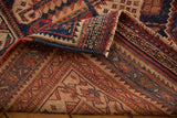 Folded corner reveals Antique Afshar rug's hand-knotted back and intricate navy, red geometric patterns.