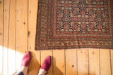 Corner view of antique Malayer rug, showing Herati motif, madder red, gold borders, and fringe.