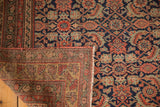 Folded antique Malayer rug corner, revealing intricate navy, red, gold Herati pattern and hand-knotted foundation.
