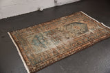 Distressed Hamadan rug corner, showing worn pile, geometric patterns, and short fringe.