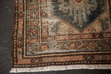 Hamadan rug corner with distressed geometric pattern, exposed foundation, faded teal, beige, and fringe.