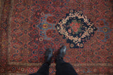 Feet on vintage Bijar rug showing madder red field, navy rose and Herati motifs.