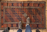 Antique Belouch rug featuring madder red, navy geometric floral panels underfoot.