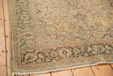 Distressed vintage Kashan rug corner, showing intricate charcoal floral border and light fringe.