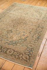Distressed vintage Kashan rug corner, displaying intricate floral border and muted tones.