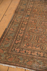 Distressed Malayer runner corner with intricate border, pale rust, blue accents, and fringe.