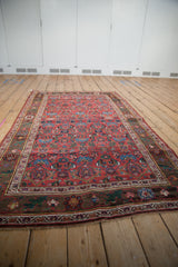 Antique rug corner: cherry red floral field, green vine border, with visible wear.