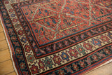 Vintage Kurdish rug corner showing a madder red field, ornate geometric borders, and secured fringe.