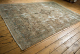 Distressed vintage Kerman carpet corner displaying muted floral vinery, worn texture, and secured edge.