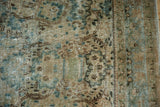 Detail of distressed Kerman carpet, showing worn pile, green-blue vinery, and visible foundation.