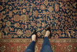 Vintage Heriz rug's intricate navy blue, madder red, and blush allover pattern; feet visible.