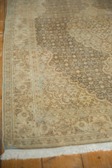 Distressed vintage Tabriz rug corner showing faded Herati motif and white fringe.
