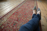 Perspective view down a distressed Persian runner highlighting its low pile and copper red color.
