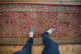 A person's view showing the scale and worn texture of a vintage Malayer runner's boteh pattern.