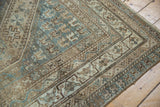 Distressed vintage Kamseh rug corner, showcasing faded beige, slate blue, and geometric borders.