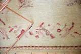 Detail of a vintage Oushak rug: ivory field, raspberry floral, serrated leaf border, and fringe.
