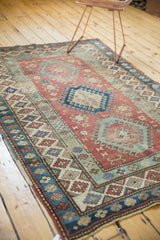 Distressed vintage Caucasian rug corner, blue and red geometric border, light fringe, worn pile.