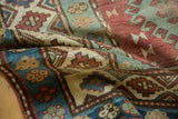 Distressed vintage Caucasian rug pile reveals geometric motifs in red, sky blue, beige.