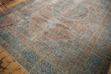 Distressed Persian Tabriz rug corner, showing faded pale blue border and floral motifs.