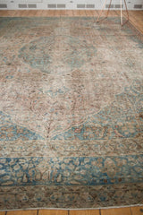 Faded curvilinear patterns in pale blue and ivory on a distressed Tabriz carpet border.