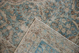 Distressed Tabriz carpet corner, worn pile with pale blue-green, beige scrolling floral motifs.