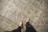 Distressed Meshed carpet with worn ivory and seafoam floral pattern under beige boots.