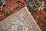 Folded vintage Qom carpet: brick red field with deer, birds, and patterned fringe edge.