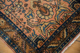 A vintage Lilihan rug corner with a navy blue border framing scrolling floral vinery.