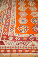 Kilim rug end with intricate geometric border in red, orange, and ivory, and fringe.