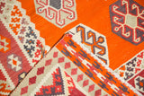 Folded vintage Turkish Kilim showing geometric gul motifs and original side cord selvage in tangerine, ivory, and raspberry.